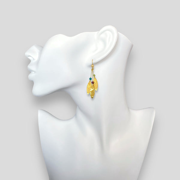 Longues boucles d'oreilles fines avec trois pointes en métal martelé doré à l'or fin et petites perles de pierres naturelles, portées à l'oreille sur fond blanc
