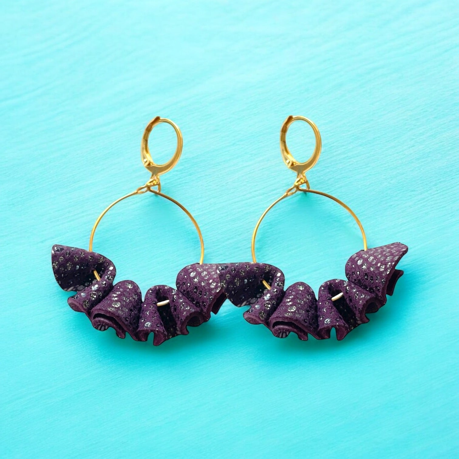 Grandes boucles d'oreilles dorées en froufrous de cuir recyclé violine mouchetée pailletée, sur fond bleu