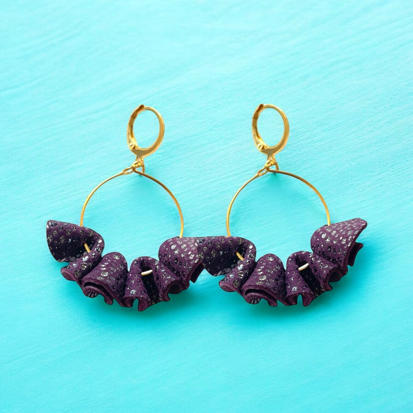 Grandes boucles d'oreilles dorées en froufrous de cuir recyclé violine mouchetée pailletée, sur fond bleu