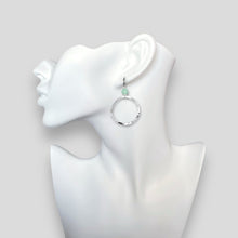 Charger l&#39;image dans la galerie, Boucles d&#39;oreilles créoles de forme ronde en métal martelé argenté et perles de fluorite vert d&#39;eau, portées à l&#39;oreille sur un buste blanc
