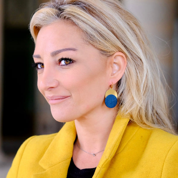 Femme blonde portant les Boucles d'oreilles dorées Nune modèle Eclipse avec disque de cuir bleu nuit sur un disque doré, vue de profil