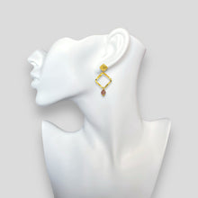 Charger l&#39;image dans la galerie, Boucles d&#39;oreilles losanges montées sur puces en métal martelé doré à l&#39;or fin et perles de quartz fraise, portées à l&#39;oreille sur un buste blanc
