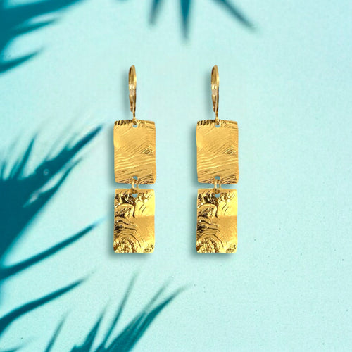 Boucles d'oreilles pendantes composées de 2 rectangles en métal martelé doré à l'or fin, sur fond bleu ombragé