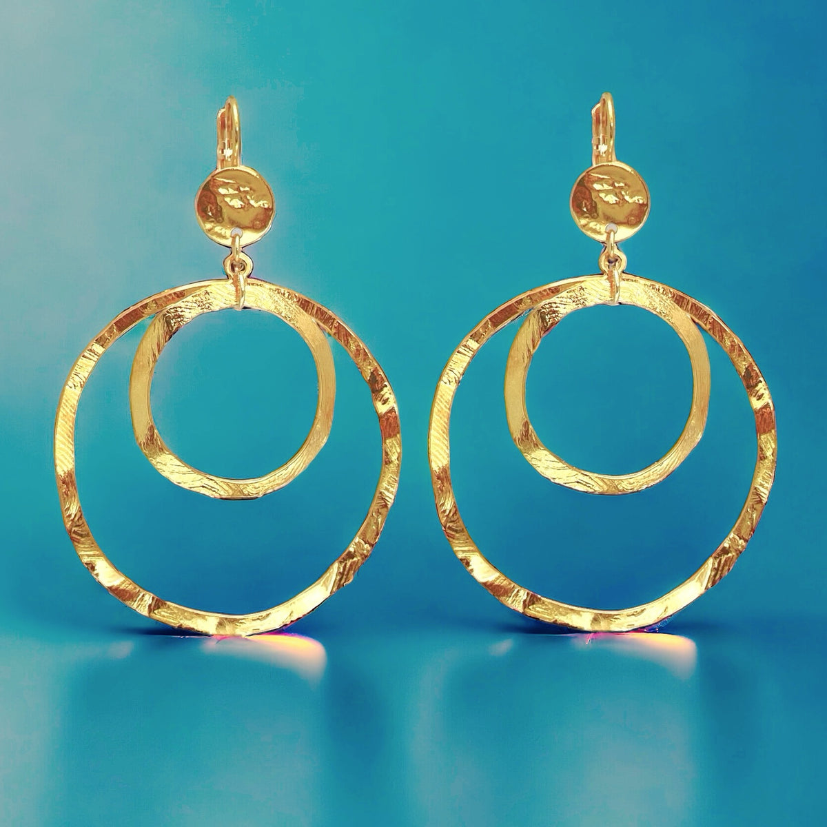 Grandes boucles d'oreilles créoles dorées à double anneau en métal martelé, avec attaches-dormeuses, sur fond bleu