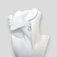 Charger l&#39;image dans la galerie, Longues boucles d&#39;oreilles argentées en métal martelé, de style ethnique bohème chic, avec leurs pampilles en forme de plumes, portées aux oreilles sur un buste blanc
