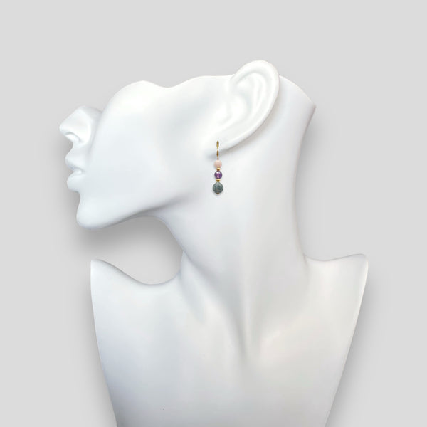 Boucles d'oreilles pendantes dorées en perles de pierres naturelles œil de chat gris, améthyste et quartz rose, portées à l'oreille sur un buste blanc