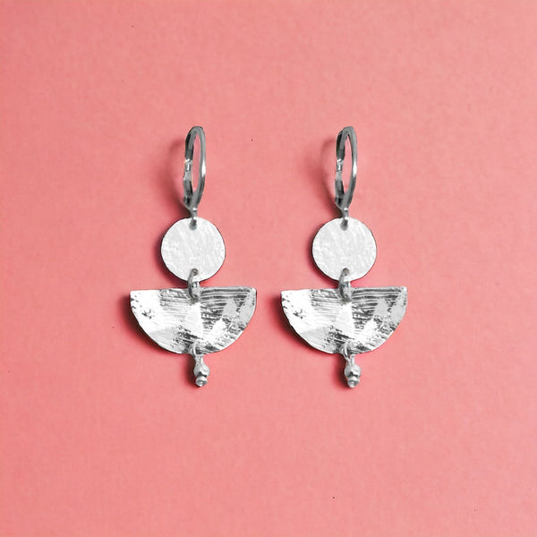 Petites boucles d'oreilles argentées pendantes en forme de demi-lunes, sur fond vieux rose