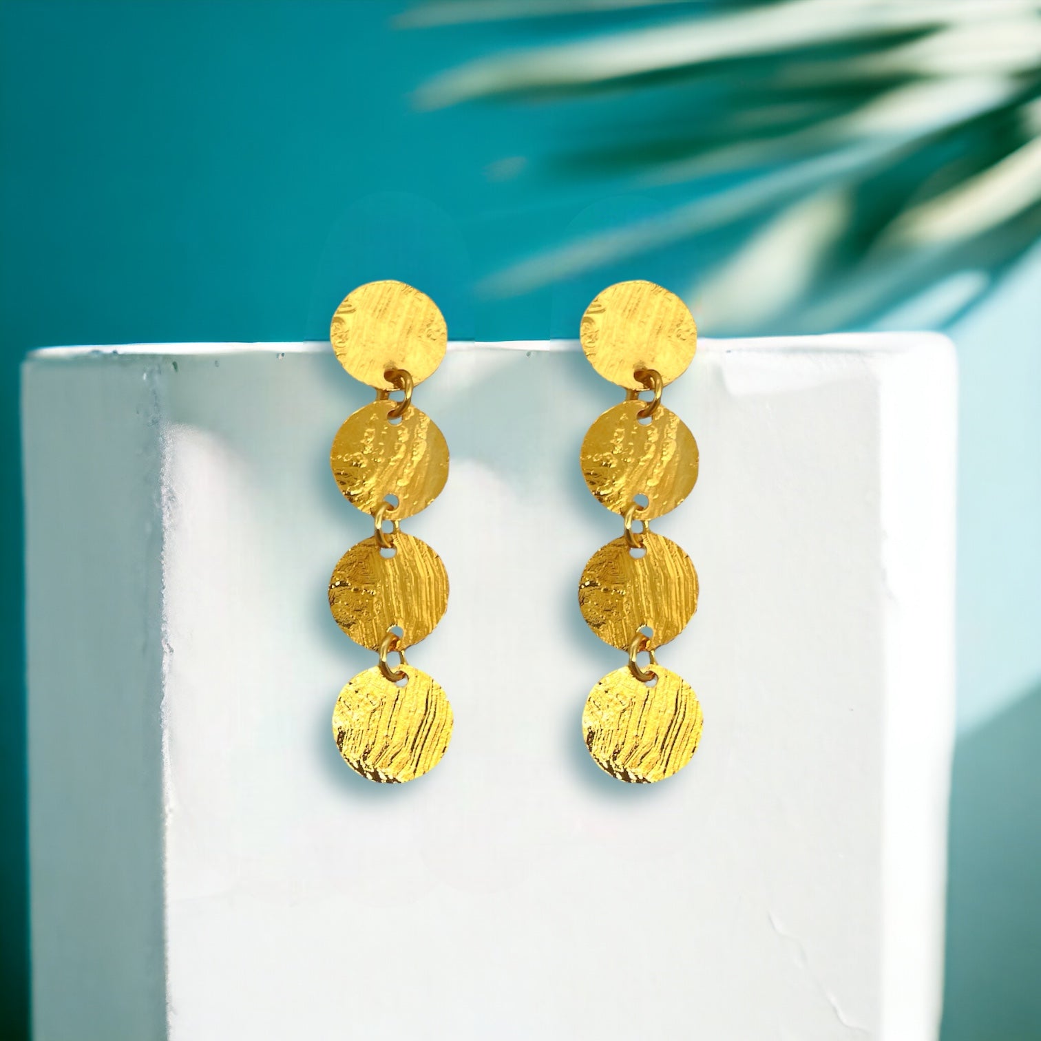 Fines puces d'oreilles pendantes en chapelet de 4 petits sequins ronds en métal martelé doré à l'or fin, sur un pot blanc, sur fond vert ombragé