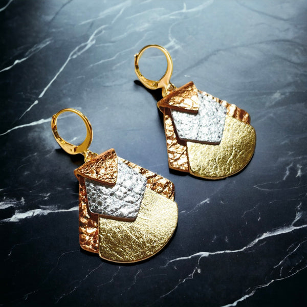 boucles d'oreilles aux formes géométriques en cuirs 3 ors, sur fond marbre noir, vues de biais 