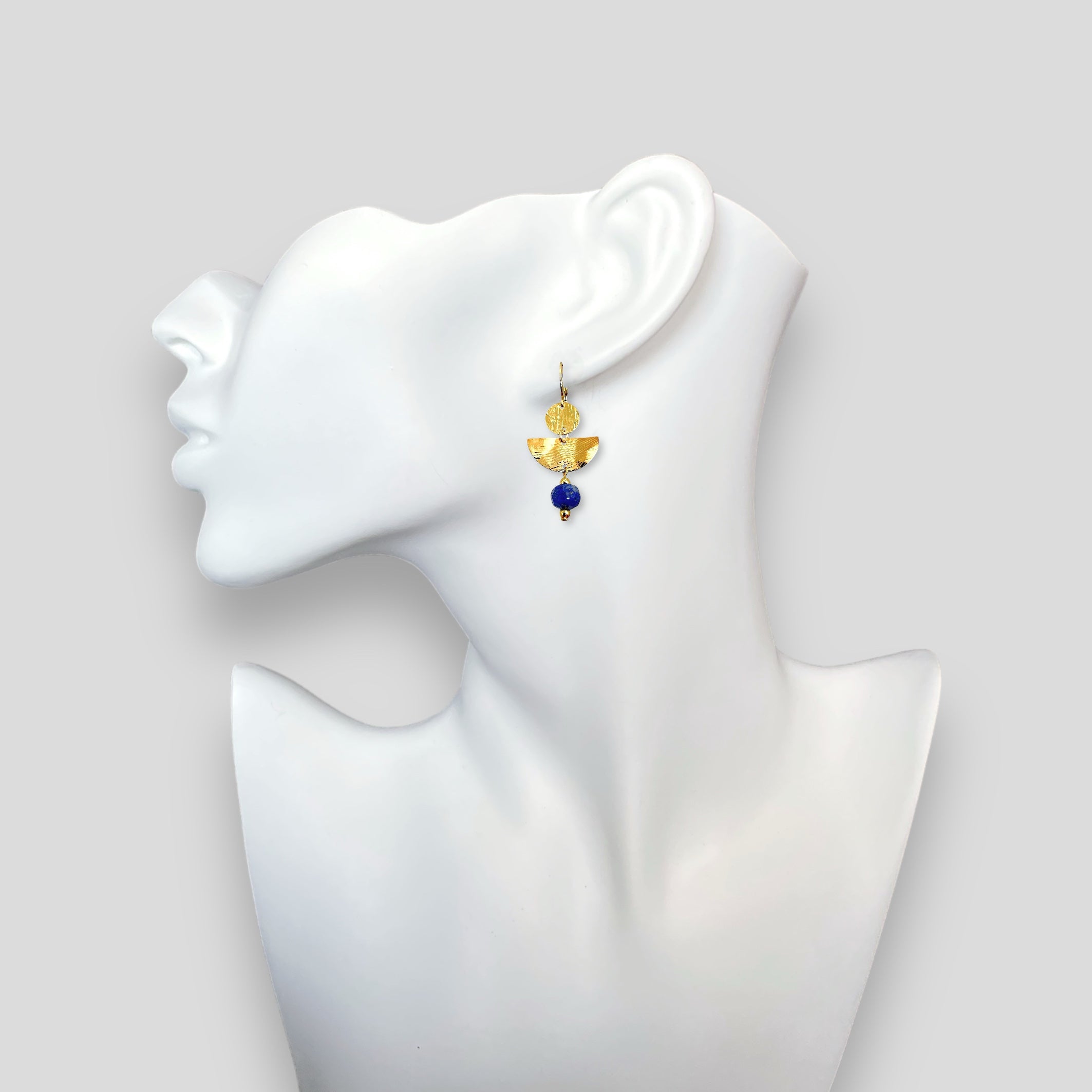 Boucles d'oreilles pendantes de forme demi-lune, en métal martelé doré à l'or fin et perles de Lapis Lazuli, portées à l'oreille sur un buste blanc