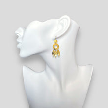 Charger l&#39;image dans la galerie, Longues boucles d&#39;oreilles dorées à l&#39;or fin en métal martelé, de style ethnique bohème chic, avec leurs pampilles en forme de plumes, portées aux oreilles sur un buste blanc
