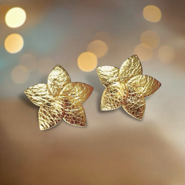 Paire de Boucles d'oreilles puces en forme de fleurs en pétales de cuir doré, sur fond beige lumineux