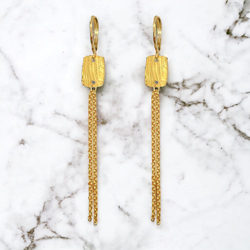 Fines boucles d'oreilles pendantes en métal martelé doré à l'or fin avec pendant rectangulaire et chainette, sur marbre blanc