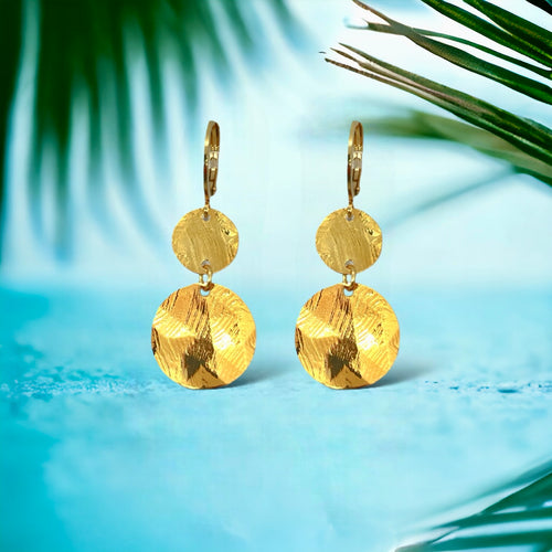 Petites boucles d'oreilles dorées pendantes avec 2 petits sequins ronds en métal martelé, sur fond bleu et feuilles de palmier