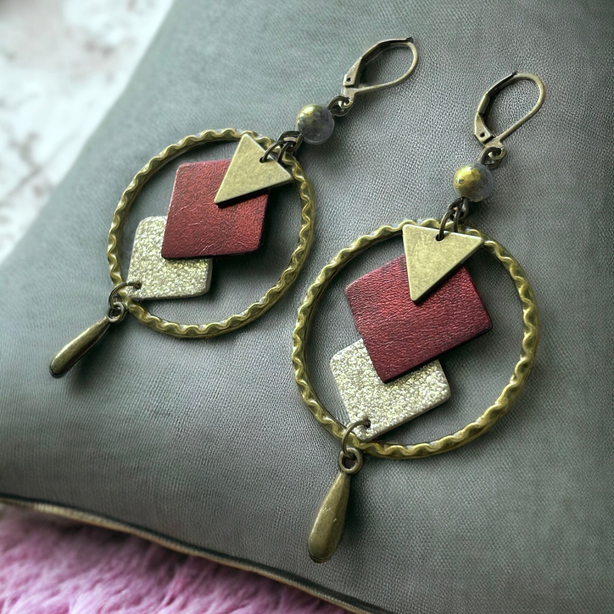 Boucles d'oreilles en bronze Nune modèle Adamante Créoles en cuir grenat métallisé e forme de losange sur fond vert kaki