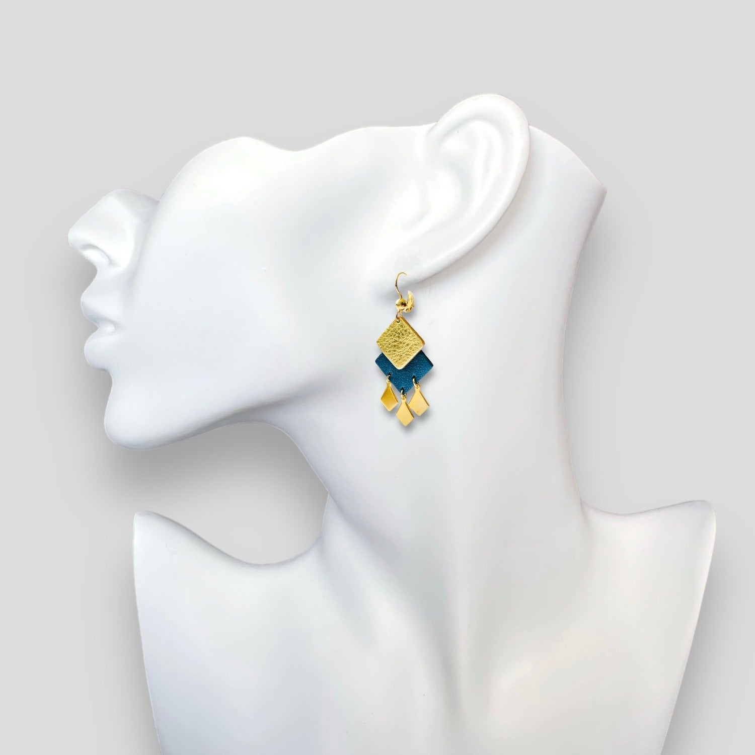 Boucles d'oreilles dorées Diamante en duo de losanges en cuirs doré et bleu nuit métallisé et pendentifs losanges dorés. Forme géométrique, style éthnique. Portée à l'oreille sur un buste blanc