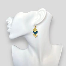 Charger l&#39;image dans la galerie, Boucles d&#39;oreilles dorées Diamante en duo de losanges en cuirs doré et bleu nuit métallisé et pendentifs losanges dorés. Forme géométrique, style éthnique. Portée à l&#39;oreille sur un buste blanc
