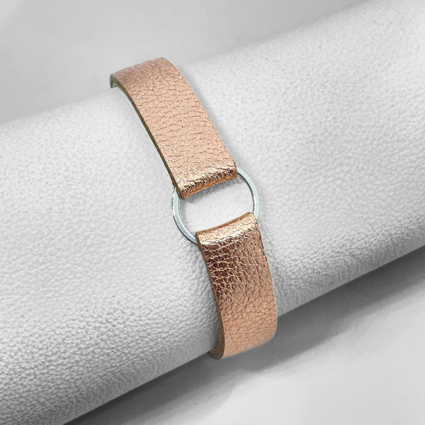 Bracelet en cuir rose pâle métallisé avec fine boucle argentée, enroulé autour d'un rouleau de cuir blanc