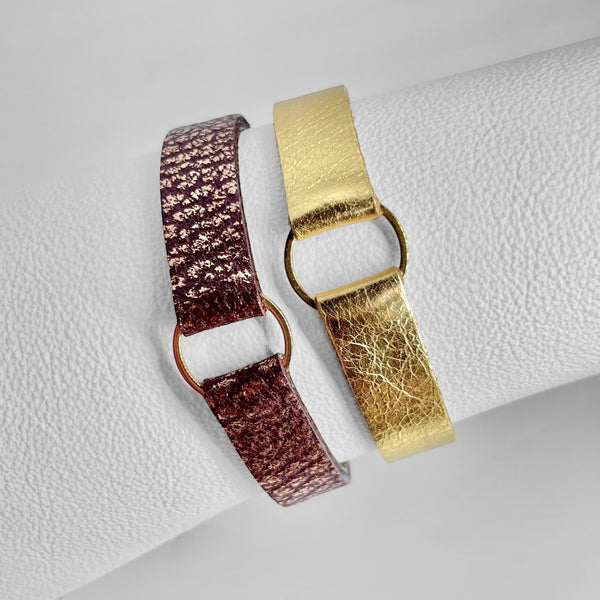 2 Bracelets en cuirs doré brillant et chocolat grainé ou rose avec fine boucle dorée, enroulés autour d'un rouleau de cuir blanc, vus de biais