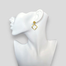 Charger l&#39;image dans la galerie, Boucles d&#39;oreilles puces dorées à l&#39;or fin en métal martelé avec pendentif en forme de losange, portées aux oreilles sur un buste blanc
