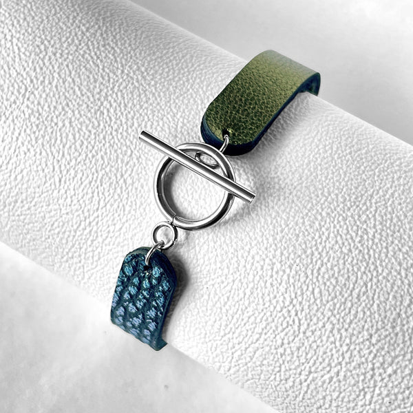 Bracelet bicolore vue de dessous, avec boucle-fermoir en T argentée, en cuirs recyclés bleu glacier métallisé grainé et kaki métallisé, enroulé autour d'un rouleau de cuir blanc