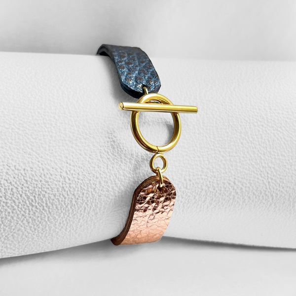 Bracelet bicolore vue de dessous, avec fermoir en T doré en cuirs recyclés or rose froissé et gris mordoré grainé, enroulé autour d'un rouleau de cuir blanc