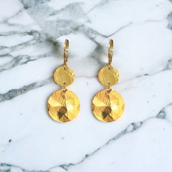 Petites boucles d'oreilles dorées pendantes avec 2 petits sequins ronds en métal martelé, sur fond marbre blanc