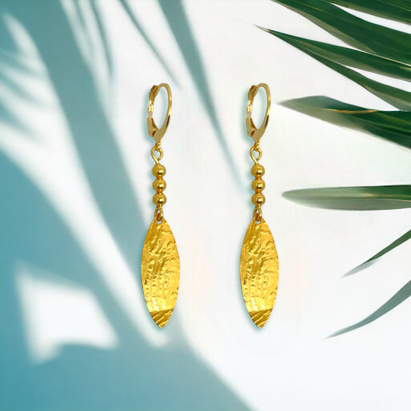 Boucles d'oreilles dorées fines pendantes en pointes, sur fond vert ombragé