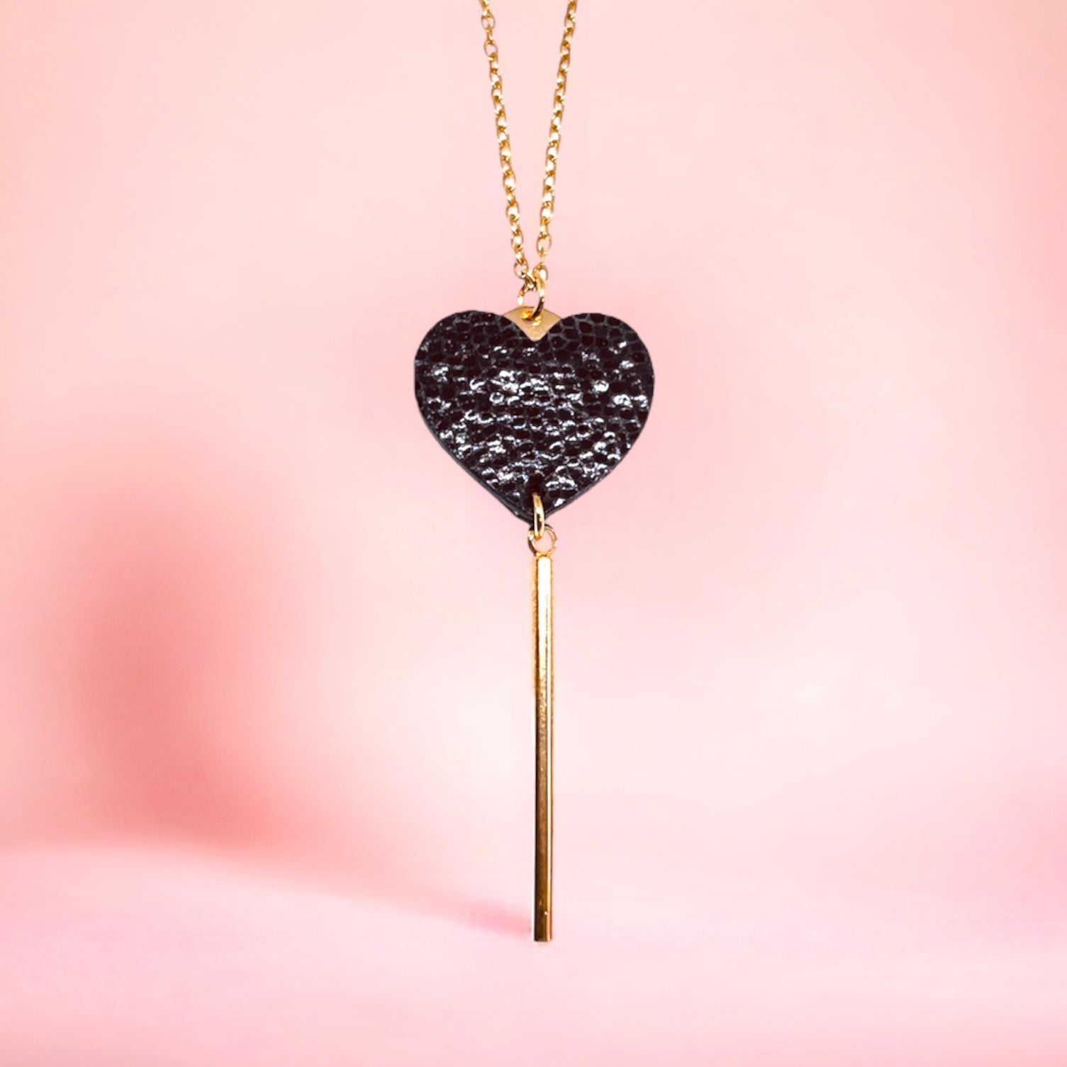 NUNE collier doré Félicie en forme de clé des cœurs cœur en cuir recyclé noir brillant façon serpent sur fond rose, vu de près