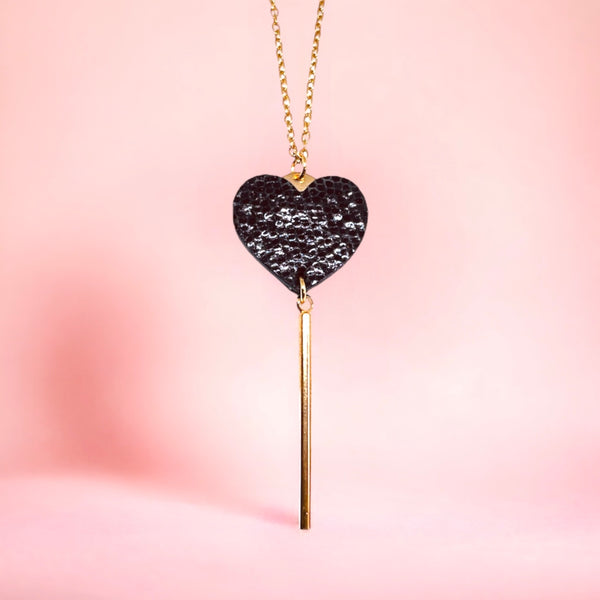 NUNE collier doré Félicie en forme de clé des cœurs cœur en cuir recyclé noir brillant façon serpent sur fond rose, vu de près