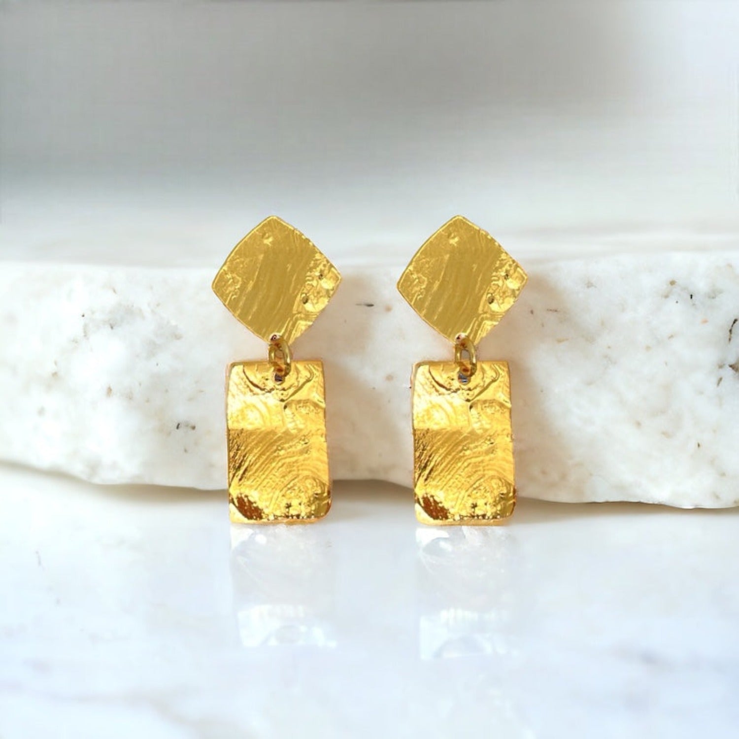 Petites puces d'oreilles losanges avec pendant rectangulaire en métal martelé doré à l'or fin, sur fond marbre blanc