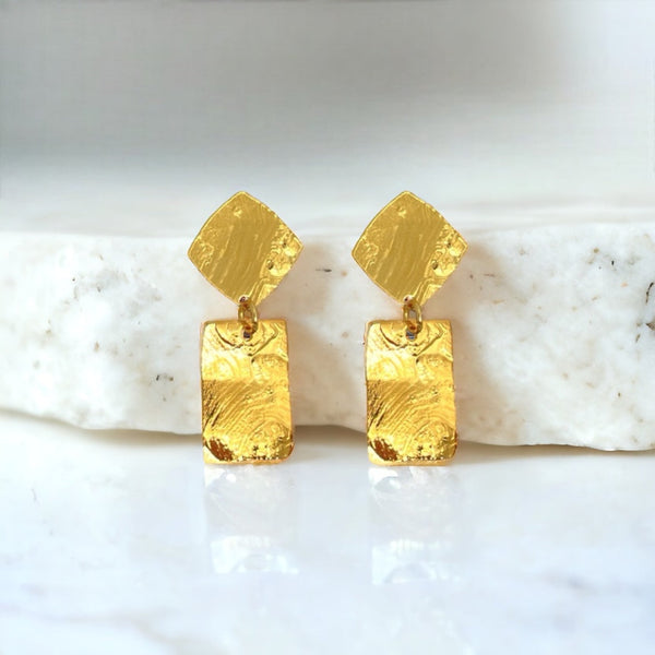 Petites puces d'oreilles losanges avec pendant rectangulaire en métal martelé doré à l'or fin, sur fond marbre blanc