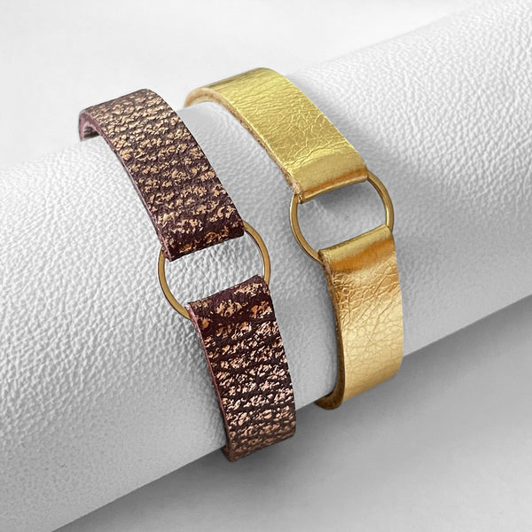 2 Bracelets en cuirs doré brillant et chocolat grainé ou rose avec fine boucle dorée, enroulés autour d'un rouleau de cuir blanc