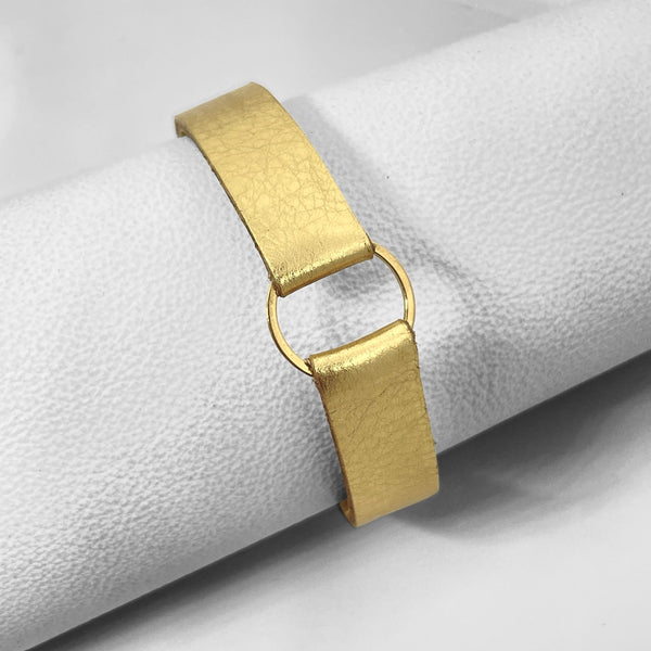 Bracelet en cuir doré brillant avec fine boucle dorée, enroulé autour d'un rouleau de cuir blanc