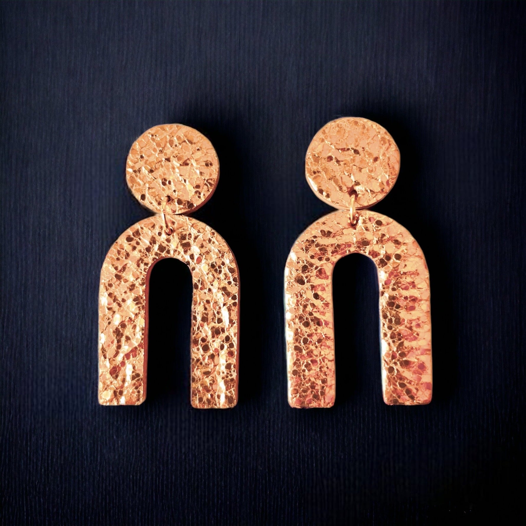 Puces d'oreilles Arkus marque Nune, en forme d'arches tout cuir or rosé froissé, sur fond noir