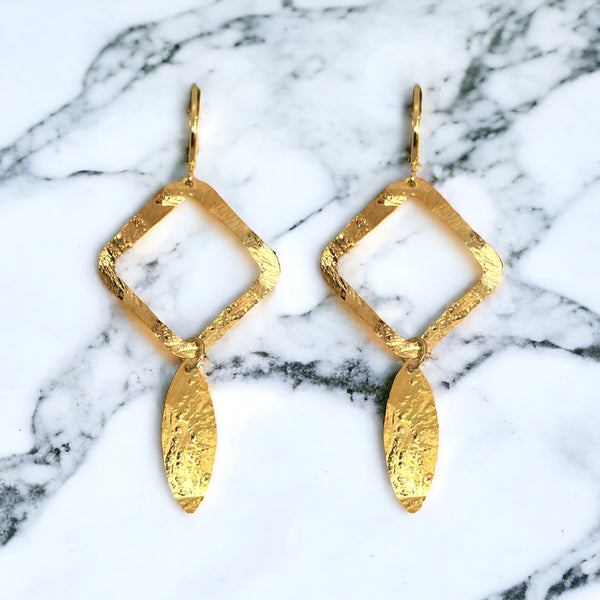 Boucles d'oreilles dorées avec pendentif en forme de losanges et pointes, sur marbre blanc