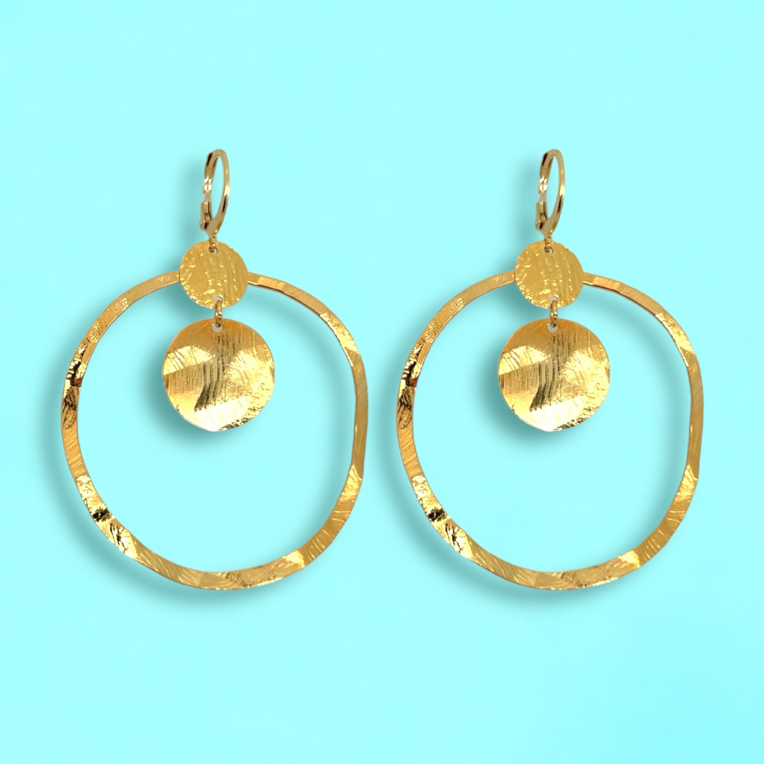 Grandes boucles d'oreilles créoles dorées avec sequins en métal martelé, avec attaches-dormeuses, sur fond bleu