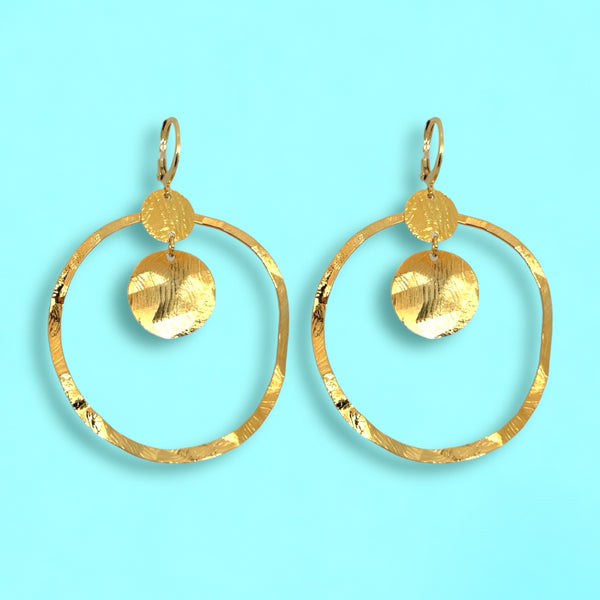 Grandes boucles d'oreilles créoles dorées avec sequins en métal martelé, avec attaches-dormeuses, sur fond bleu