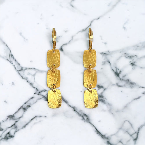 Fines boucles d'oreilles dorées pendantes en chapelet de 3 petits rectangles, sur marbre blanc