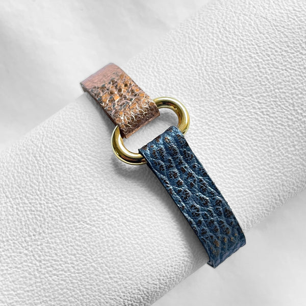 Bracelet bicolore à boucle dorée en cuirs recyclés or rose froissé et gris mordoré grainé, enroulé autour d'un rouleau de cuir blanc