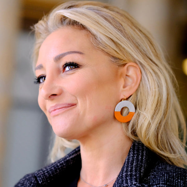 Femme blonde portant les boucles d'oreilles, rondes en forme d'anneaux bicolores en cuirs argent et orange grainé