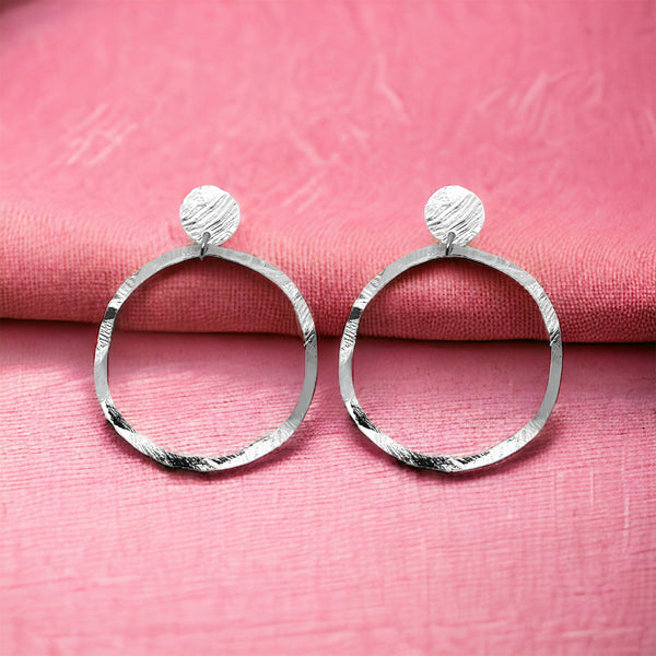 Grandes boucles d'oreilles créoles argentées en métal martelé, montées sur puces rondes, sur tissu rose