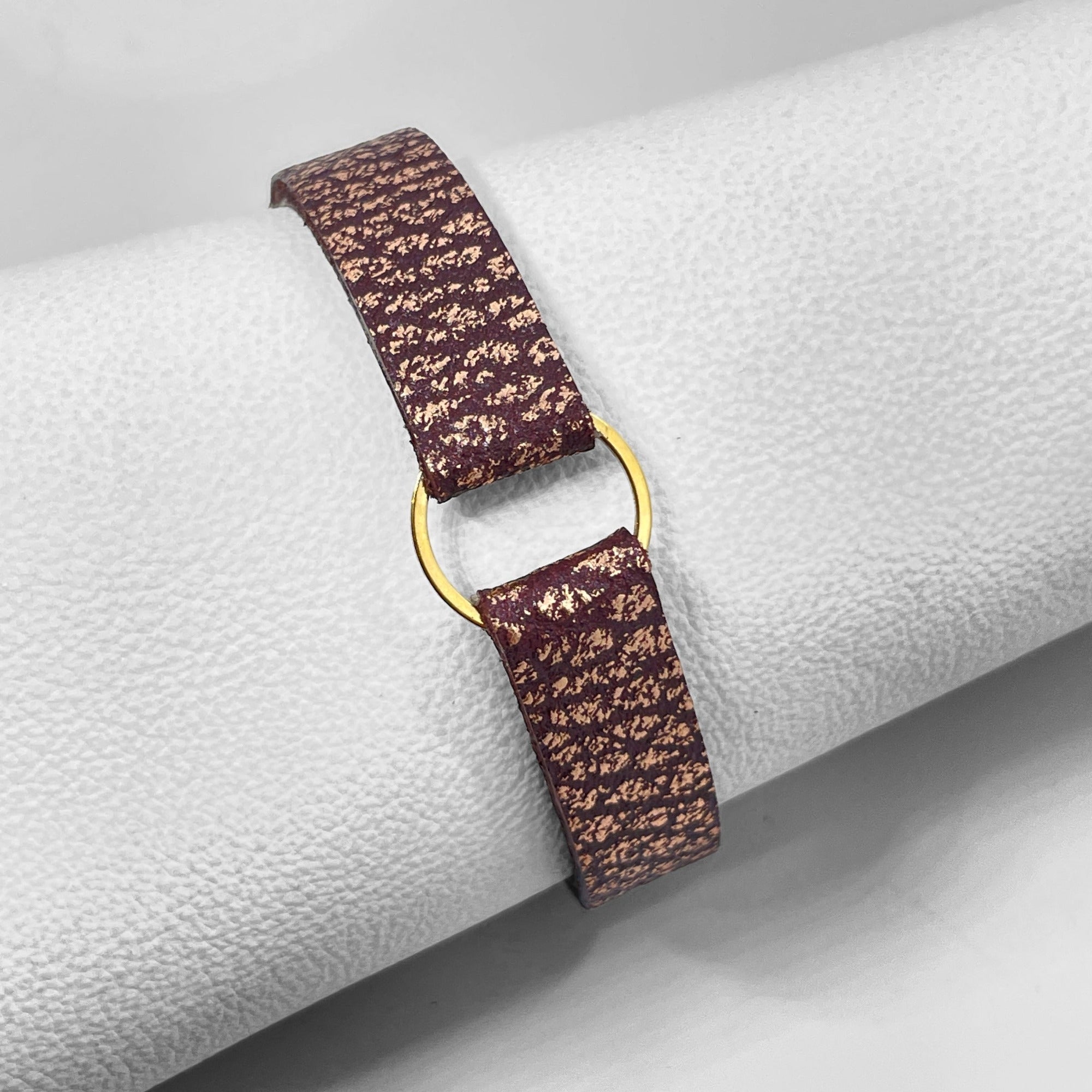 Bracelet en cuir chocolat grainé or rose avec fine boucle dorée, enroulée autour d'un rouleau de cuir blanc