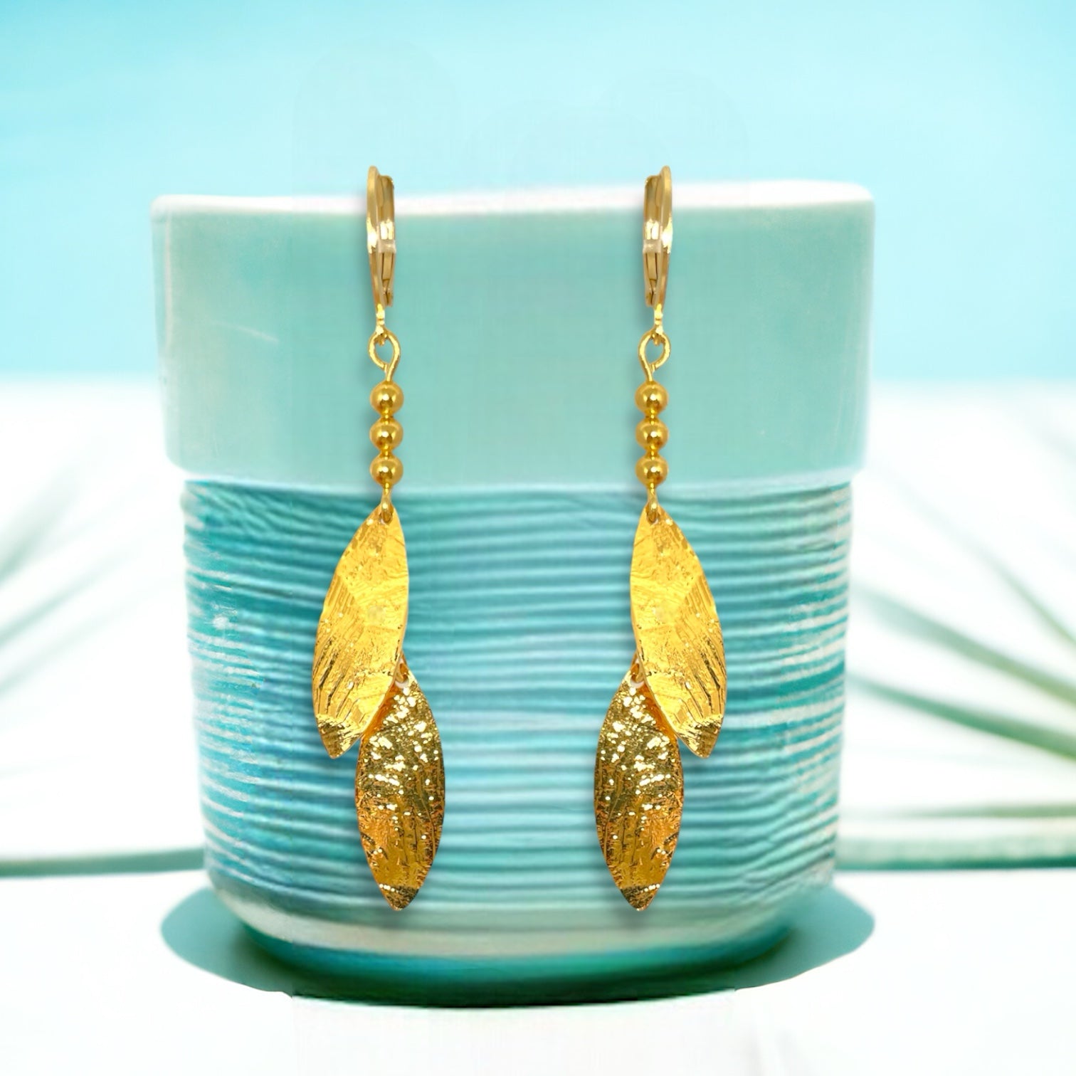 Longues boucles d'oreilles fines avec double pointes en métal martelé doré à l'or fin, sur un pot vert