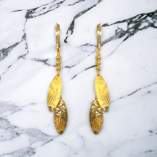 Longues boucles d'oreilles fines avec double pointes en métal martelé doré à l'or fin, sur marbre blanc