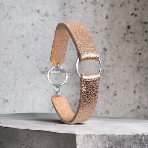 Bracelet en cuir rose pâle métallisé avec fine boucle argentée, vu en entier , sur fond béton gris 