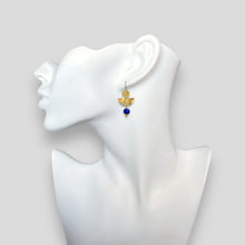 Charger l&#39;image dans la galerie, Boucles d&#39;oreilles pendantes de forme demi-lune, en métal martelé doré à l&#39;or fin et perles de Lapis Lazuli, portées à l&#39;oreille sur un buste blanc
