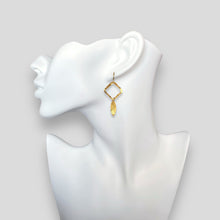 Charger l&#39;image dans la galerie, Boucles d&#39;oreilles dorées avec pendentif en forme de losanges et pointes, portées aux oreilles sur un buste blanc
