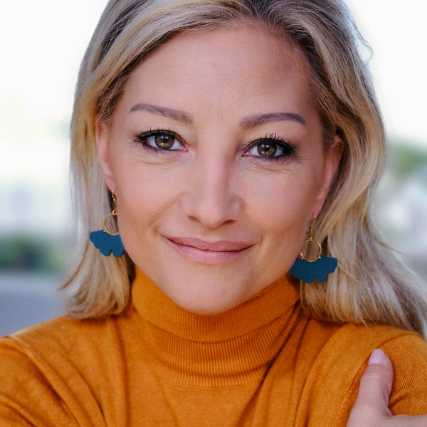 Femme blonde portant une paire de boucles d'oreilles dorées en forme de feuille de gingko en cuir vert canard