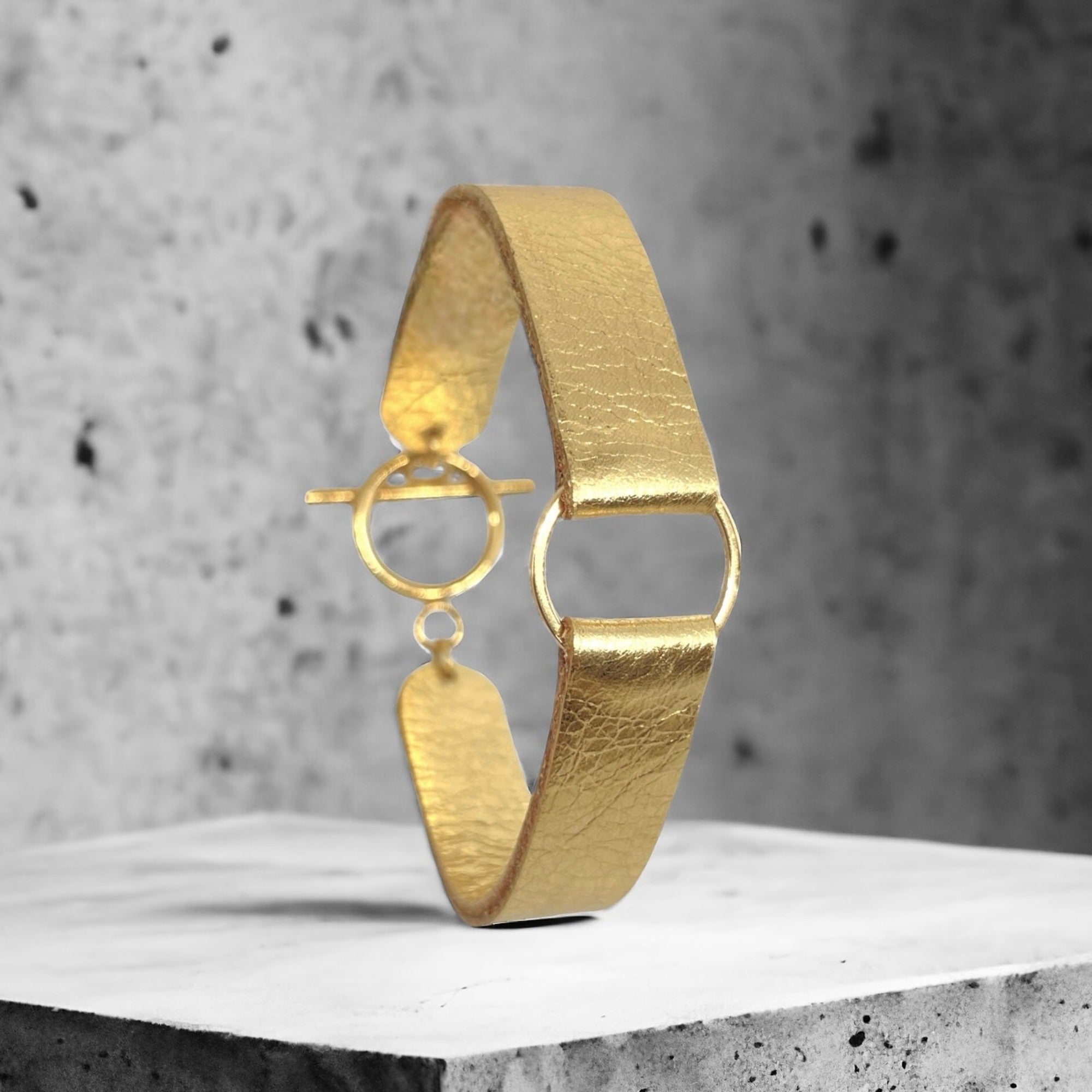 Bracelet en cuir doré brillant avec fine boucle dorée, vu en entier sur fond béton gris